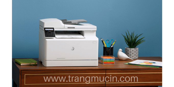 đặt máy in laser hp color laserjet pro mfp m183fw lên bàn làm việc cạnh cái kéo và chậu cây