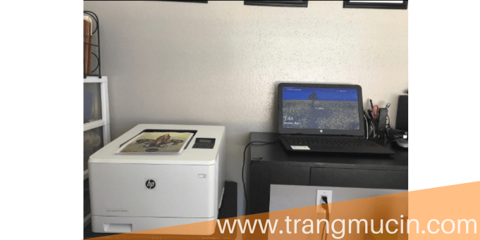 đặt máy in hp color laserjet 454nw bên cạnh bàn làm việc có máy   